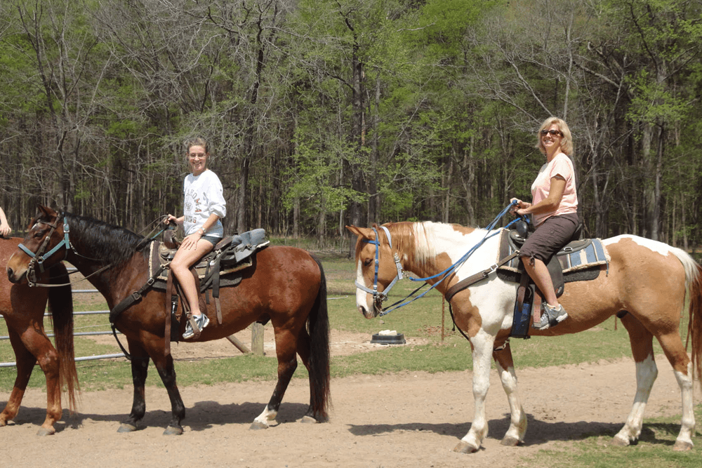 Two women are riding horses in a wooded area.