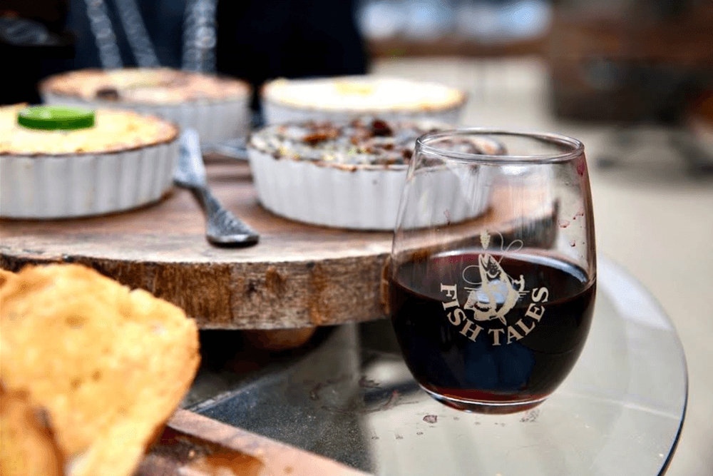 A glass of red wine sits next to several baked dishes on a wooden serving platter.