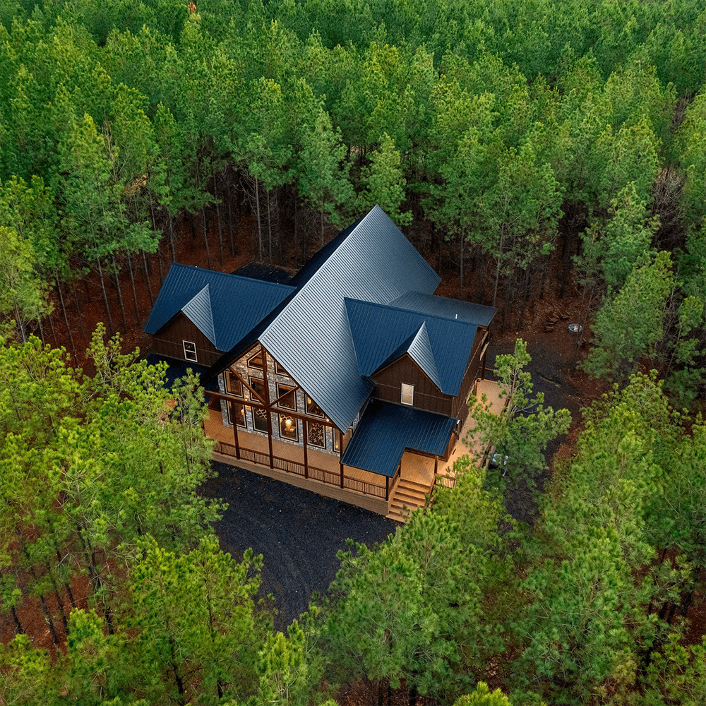 Aerial view of a modern cabin surrounded by dense green pine trees.